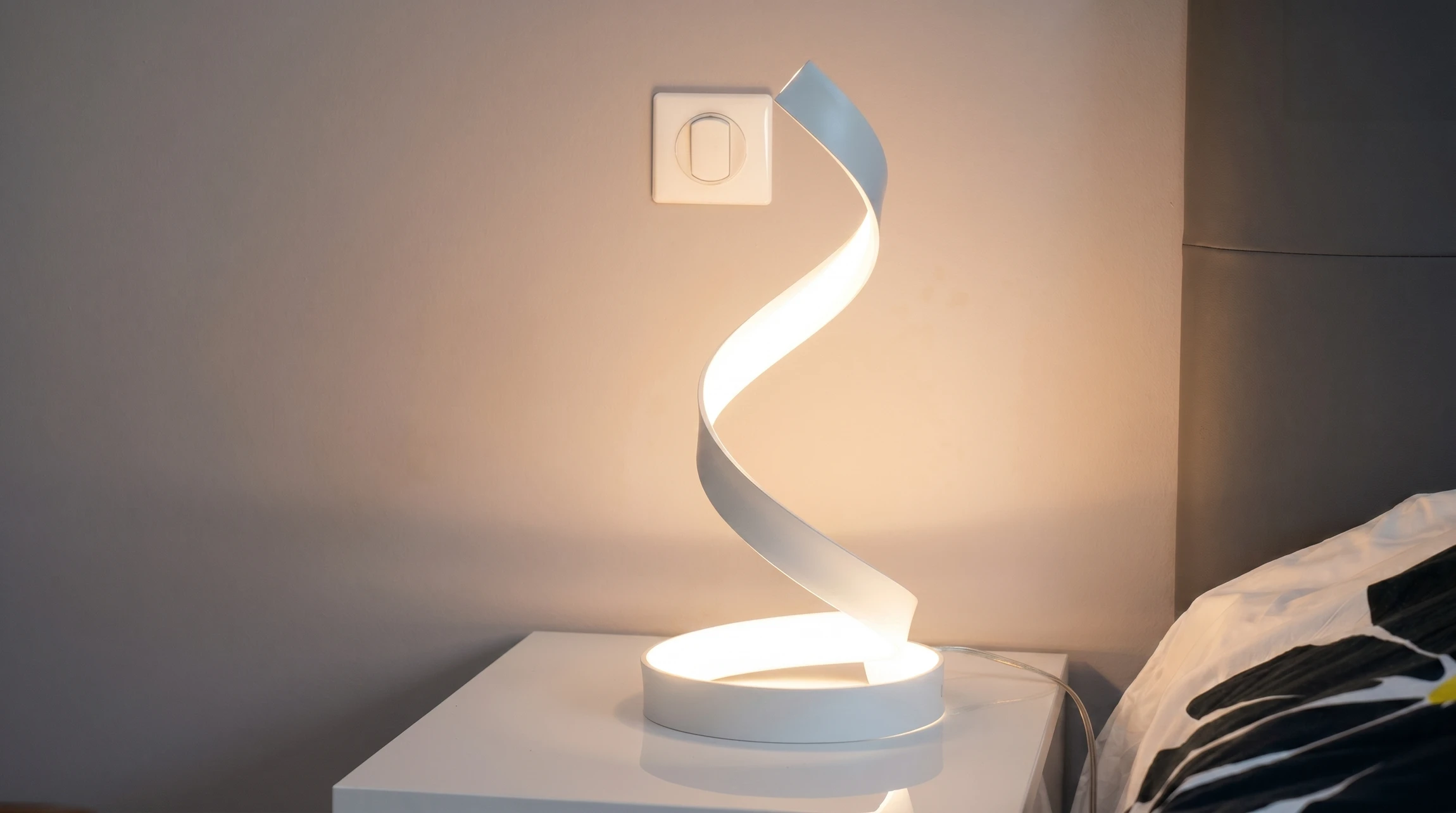 Lampe de chevet design LED en spirale hélicoïdale blanche, posée sur une table de nuit blanche dans une chambre