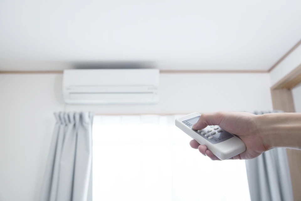 Scène intérieure résidentielle avec personne tenant une télécommande de climatisation dirigée vers une unité de climatisation murale