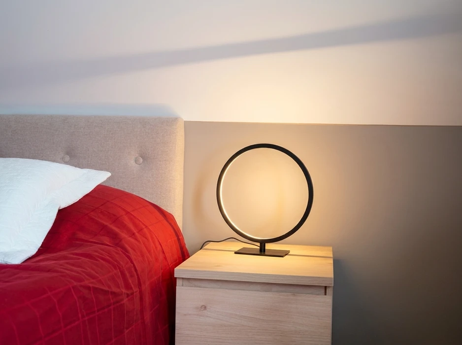 Chambre à coucher moderne, table de chevet en bois clair avec lampe LED circulaire design, anneau lumineux noir émettant une lumière chaude dorée