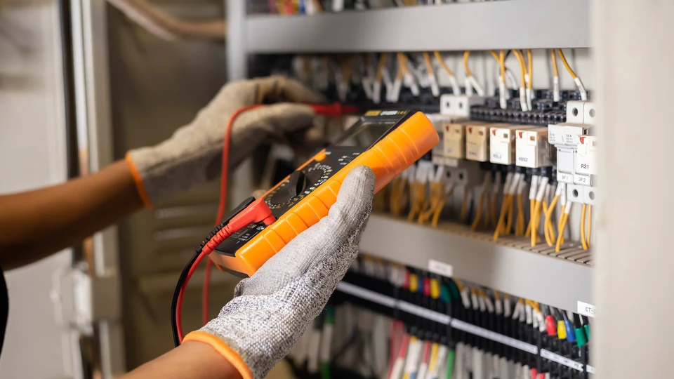 Un ingénieur électricien utilise un multimètre pour tester l'installation électrique et le courant de ligne électrique dans une armoire de commande de système électrique