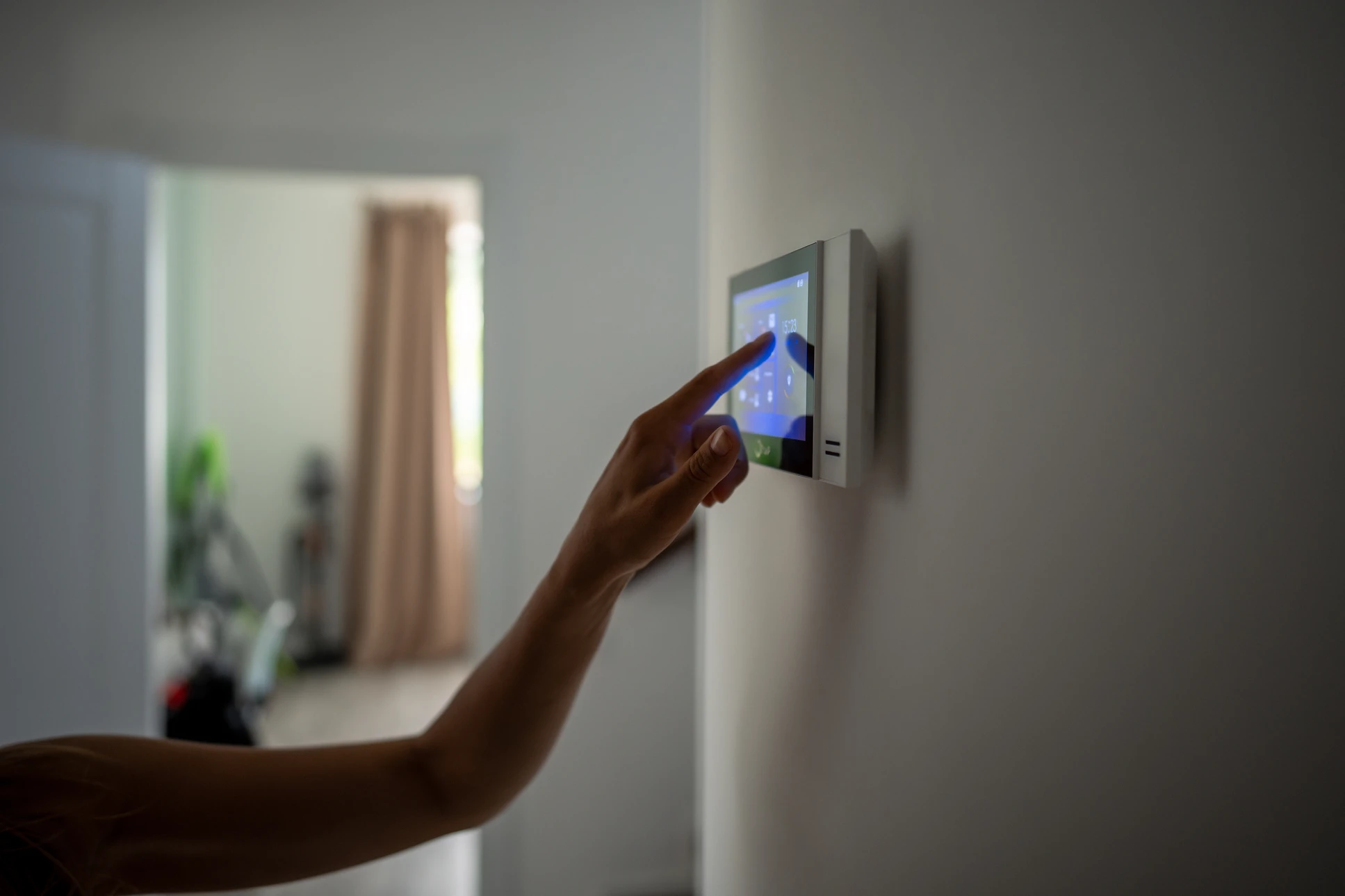 Photographié en plan large d'un intérieur résidentiel moderne, un technicien professionnel en uniforme bleu intervient dans un salon lumineux. Il installe ou vérifie une borne de recharge murale pour véhicule électrique. Au second plan, légèrement flou, on distingue une pompe à chaleur moderne fixée au mur ou une unité intérieure de chauffage. La scène doit transmettre la polyvalence de l'entreprise : expertise électrique (borne), thermique (PAC), et professionnalisme. Pas de texte, logo ou filigrane visible.